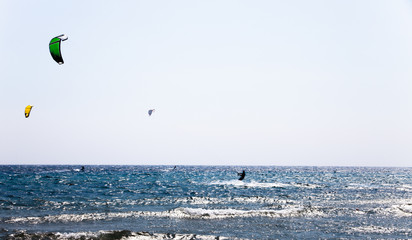 Sunny day on the blue sea with blue sky. Surfers with parachutes on the sea waves. Action sport with parachutes and surfing boards. Beautiful sunny day on the sea.