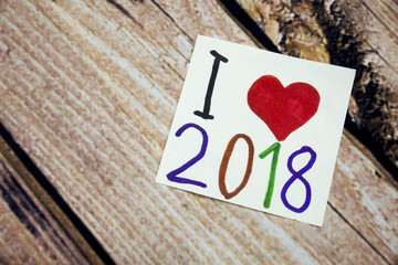 I love 2018 year with red heart symbol. Handwritten message on the white paper with wooden bark in the background. Positive concept with 2018 word on the paper.