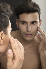MAN PUTTING ON FACE CREAM LOOKING IN THE MIRROR