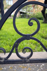 Forged elements of a fence against a background of green grass