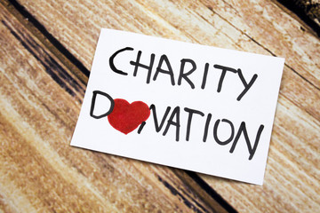 Conceptual image with Charity Donations handwritten message on the white paper with wooden background. Health and god will concept with red heart. Help for people having no money.