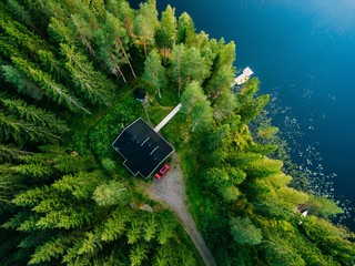 Fototapeta premium Aerial view of wooden cottage in green forest by the blue lake in rural summer Finland