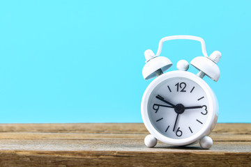 White small alarm clock on a wooden shelf on a blue pastel background. Minimalism