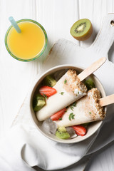 Fruit ice pops with strawberry and kiwi in bowl on table with orange juice