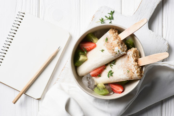 Delicious ice pops with blank notepad on wooden background