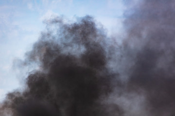 Black smoke against a blue sky with clouds
