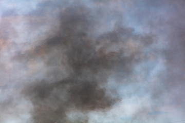Black smoke against a blue sky with clouds