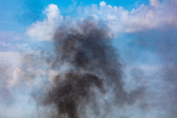 Black smoke against a blue sky with clouds