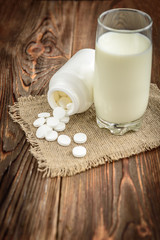 Calcium supplement tablet pills on dark wooden background. White tablets near the inverted jar and glass of milk. Pills or food concept.