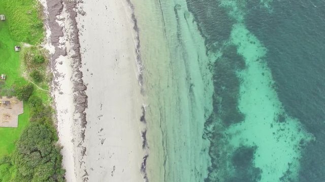Slow aerial descend looking down at beautiful sandy beach and calm turquoise shallow ocean waters