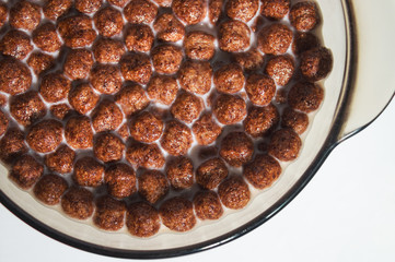Dry healthy chocolate breakfasts in the form of balls in a plate of milk. Flakes of wheat and corn