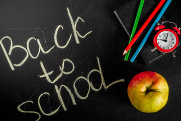 Back to school concept with books, alarm clock, color pencils, chalkboard background