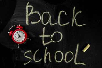 Fototapeta na wymiar Back to school concept with books, alarm clock, color pencils, chalkboard background