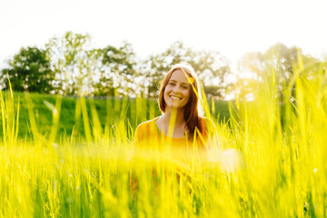 Young woman sitting laughing in the grass in the sunshine