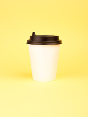 Paper coffee cup on yellow pastel colorful paper flat lay background. Takeaway drink container. Template of drink cup for your design for put text, image, and logo mockup