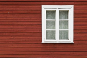 Fototapeta na wymiar White window covered with lace curtains on red wooden wall, in Estonia.