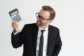 Smiling business man holding, showing calculator display and looking at it. Calculation concept. Isolated front view on white background. - obrazy, fototapety, plakaty