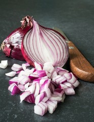 Chopped up red onions with knife on a dark stone surface