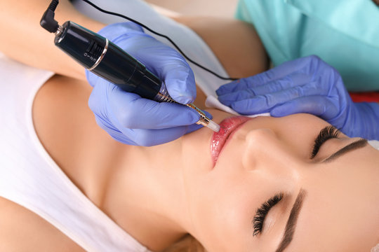 Cosmetologist making permanent makeup on woman's lips