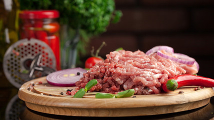 Raw chopped meat. Knife and grill from meat grinder, olive oil, spices, cherry, chili pepper, black pepper lie on a wooden board. Ready for cooking.