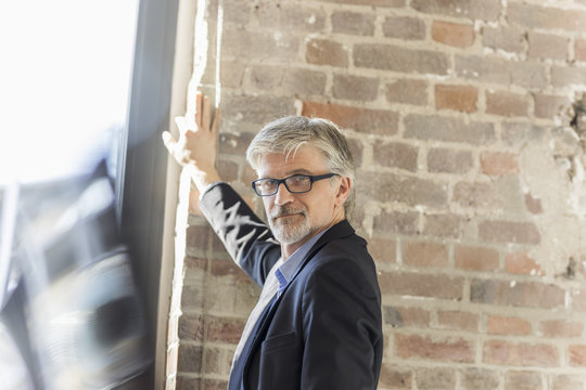 Mature businessman leaning on brick wall in office