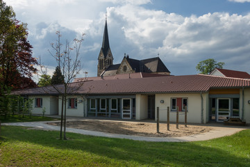 Kindergarten-Neubau in kirchlicher Trägerschaft vor Kirche - obrazy, fototapety, plakaty