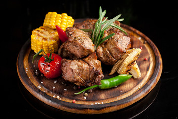 Fried meat, shish kebab, greens, parsley, dill, olive oil, iron skewers, lie on a wooden round board. Meat-eating concept.