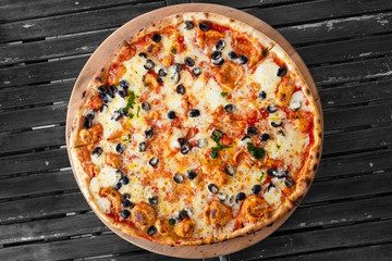 Large margherita pizza with black olives isolated on grey wood table from above.