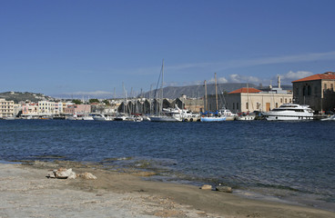 The landscape with the stone shore of Mediterranean sea, boats, houses on the coast and far mountains on the sunny day in Chania, Crete, Greece. 