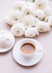 Fototapeta na wymiar Delicious fresh morning espresso coffee with a beautiful crema ob the pastel pink table background with some marshmallows on the side and tender white blossoming ranunculus flowers, top view, flat lay