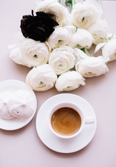 Delicious fresh morning espresso coffee with a beautiful crema ob the pastel pink table background with some marshmallows on the side and tender white blossoming ranunculus flowers, top view, flat lay