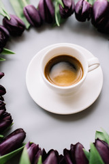 Delicious fresh morning espresso coffee with a beautiful crema and black tulips surrounding it in a circle, top view, flat lay