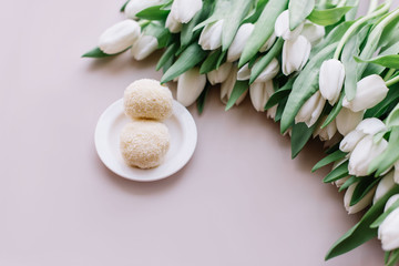 Obraz na płótnie Canvas Delicious white chocolate balls dessert and a big bunch of white tulips on the pastel pink table background