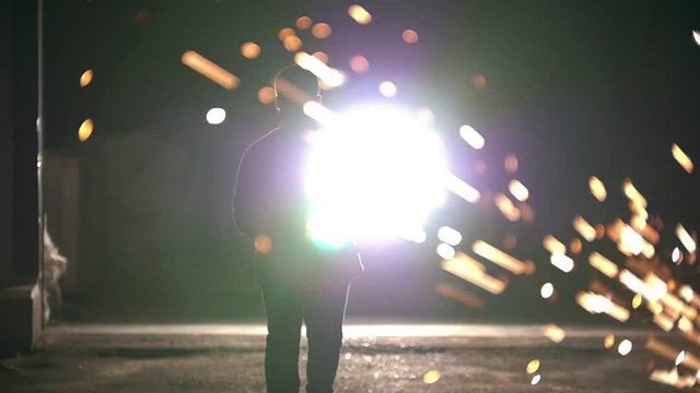Man walking among the flying sparks from grinder at night, slow-motion