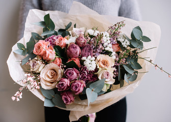 Naklejka premium Młoda kobieta kwiaciarnia gospodarstwa świeżo wykonane bukiet kwitnących kwiatów róż i eukaliptusa na tle szarej ściany.