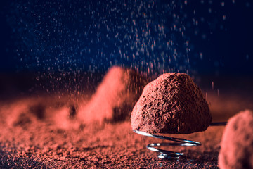 Chocolate truffles and falling cocoa powder on blue background, macro. delicious homemade truffle...