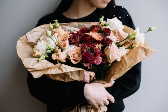 Fototapeta Young florist woman hugging freshly made blossoming flower bouquet of roses,eustoma, chrysanthemums in brown colors on the grey wall background.