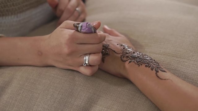 close up shot of a young woman's hands, a tattoo artist draws a floral henna pattern for a friend, the women's hands are on a pillow for the convenience of drawing patterns