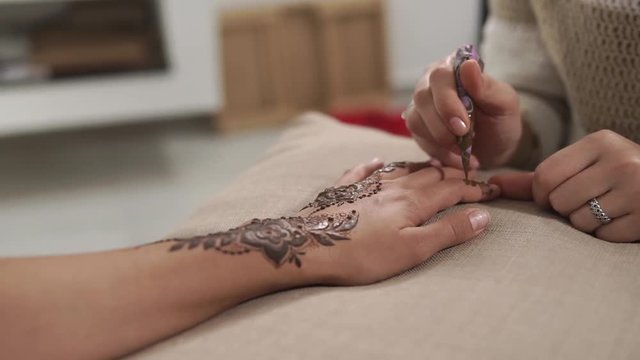 Close up shot of a process of applying henna on woman's hand and fingers. Beautiful mehndi desing. Traditional body art.