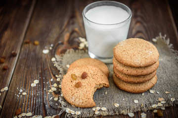 Homemade oatmeal cookies with raisins, cinnamon with milk on dark wooden background.