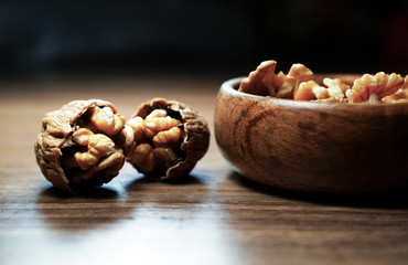 Kernel walnuts in wooden bowl with two broken walnuts on dark walnut table background.