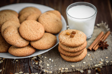 Homemade oatmeal cookies with raisins, cinnamon with milk on dark wooden background.