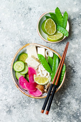 Vegan asian udon noodles soup bowl with ginger and mushrooms broth, tofu, snap peas, zucchini,...