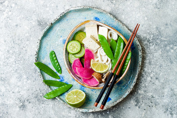 Vegan asian udon noodles soup bowl with ginger and mushrooms broth, tofu, snap peas, zucchini,...