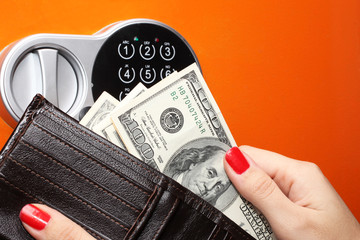 The female hand pulls out money from a wallet on the background of a digital lock safe