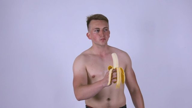 A young sexy guy is eating a banana.  
