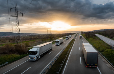 Caravan or convoy of white trucks in line on a country highway at sunset