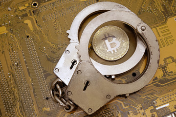 Concept fraud with crypto currency. Fraud and deception of electronic criminals and hackers. Coin bitcoin and police handcuffs lie on a yellow motherboard computer board.