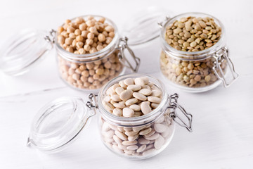 Dried Lentils Chickpeas White beans in Glass Jars on White Wooden Background Above Close Up