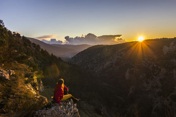 girl sitting on a cliff in mountains at sunset